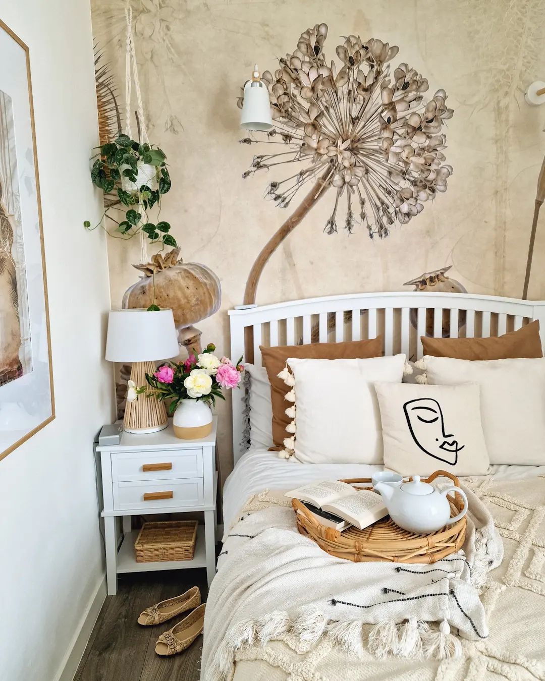 Cozy bedroom with white bed, nightstand, and floral wallpaper. A tray with a book and teapot sits on the bed.