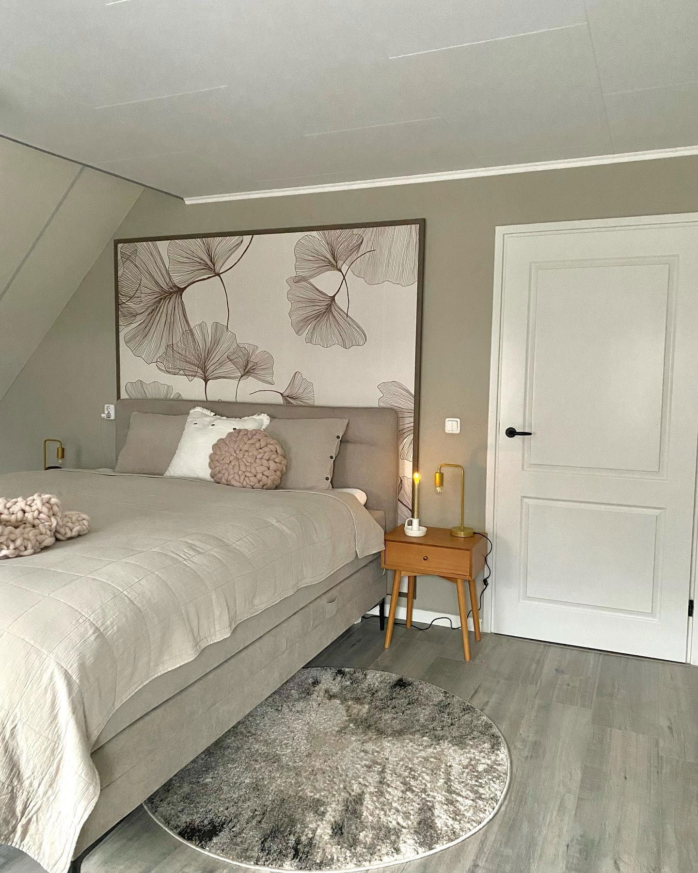 Bedroom with beige bedding, floral wall art, and wood nightstand with gold lamps.