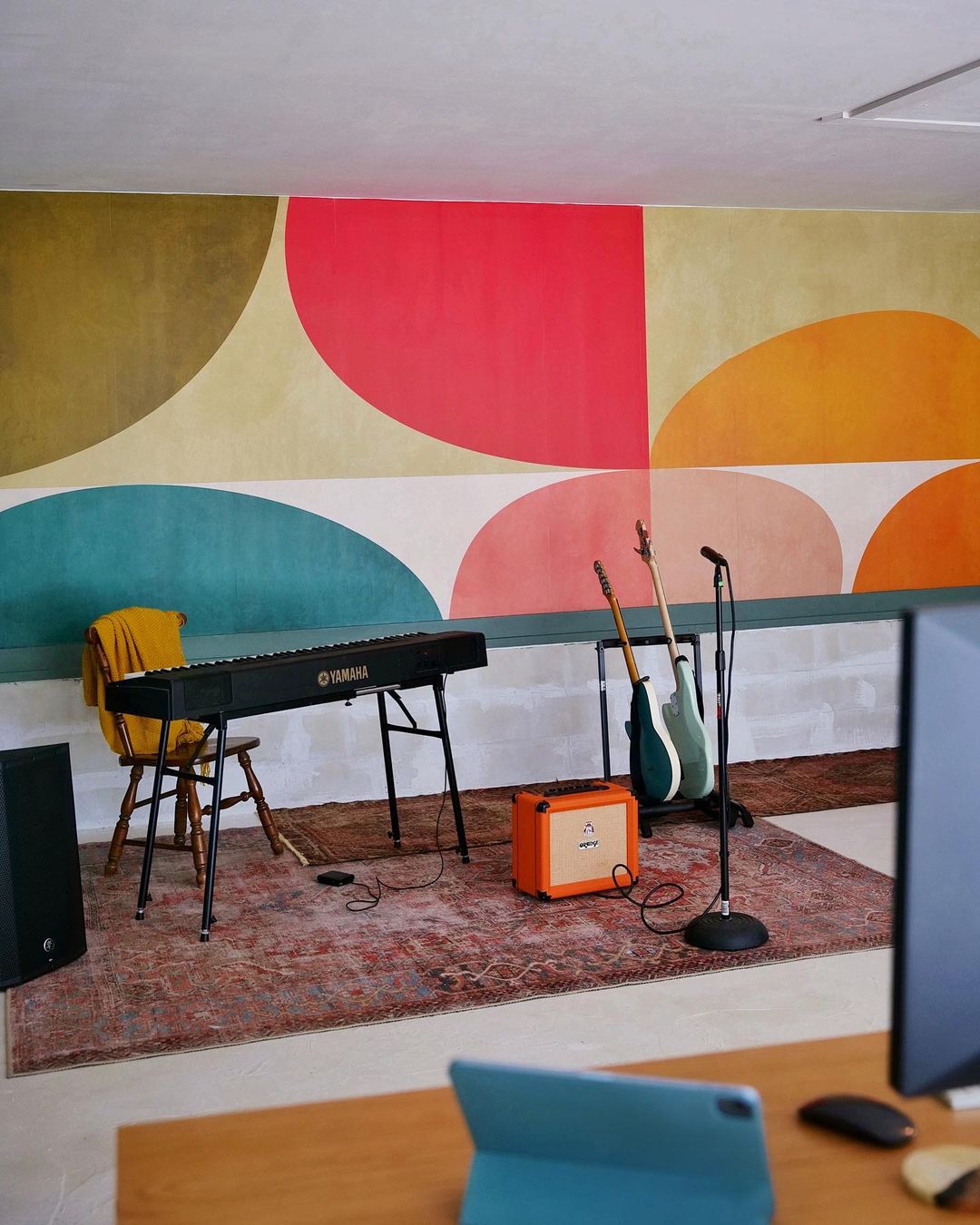 Studio de musique avec clavier Yamaha, guitares, ampli Orange et art mural géométrique coloré.
