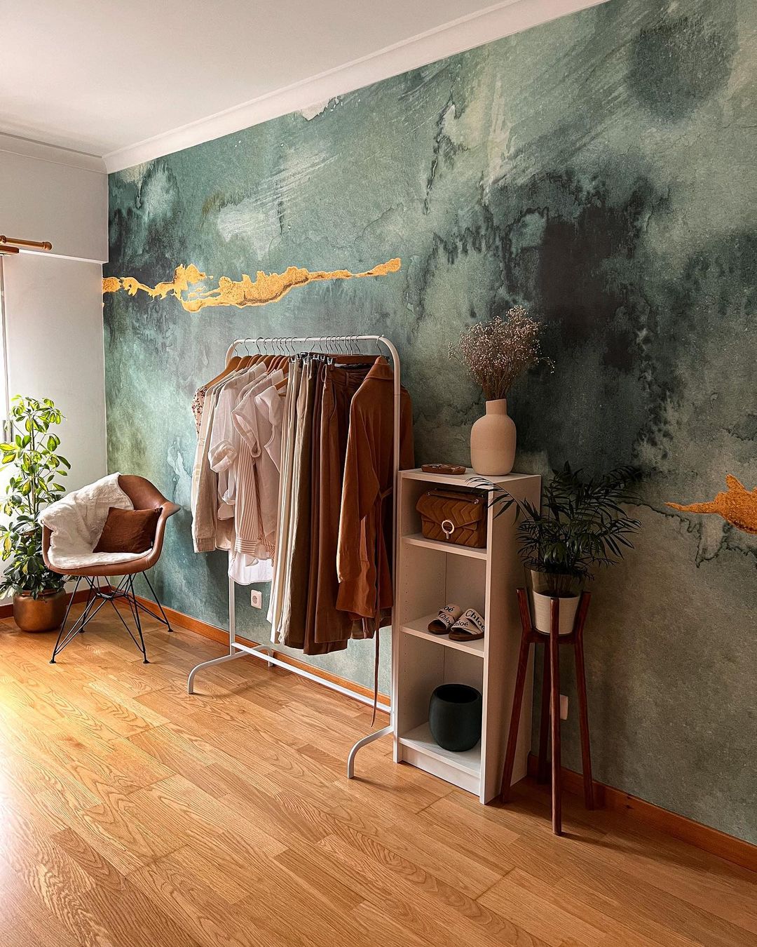 Interieur met kledingrek, stoel en schappen tegen een groene en gouden waterverfmuur.