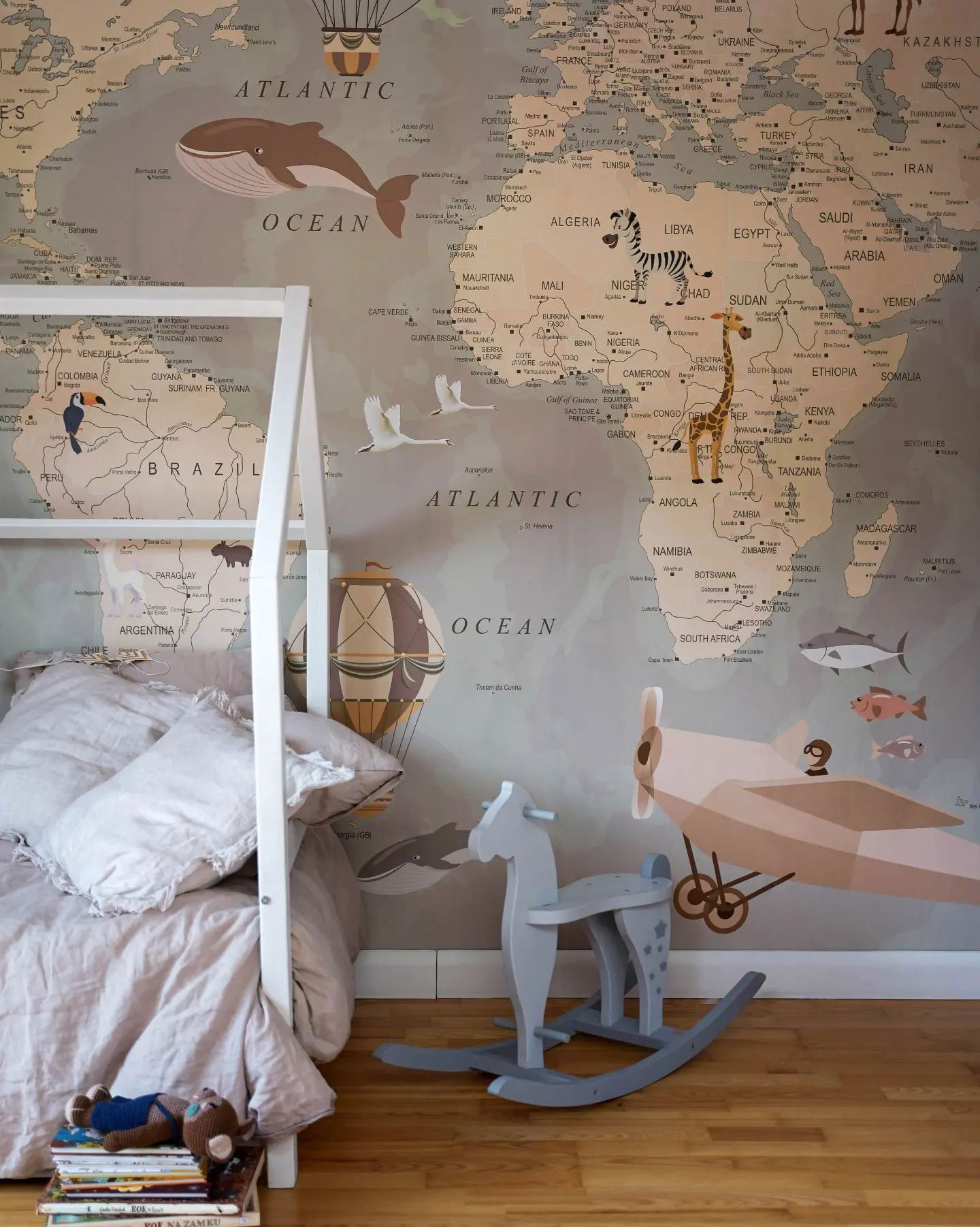 Stanza di un bambino con carta da parati con mappa del mondo raffigurante animali, mongolfiere e un aereo d'epoca. Un cavallo a dondolo è seduto vicino a un letto.