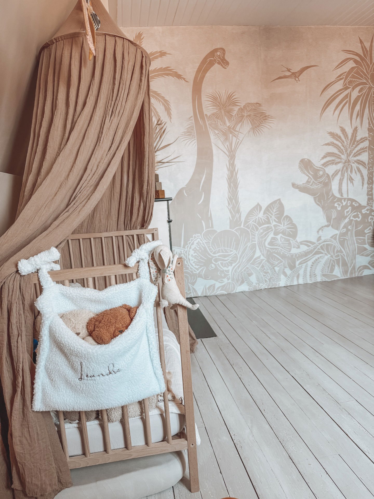 Crédence neutre avec fresque de dinosaures, berceau avec peluches et auvent beige.