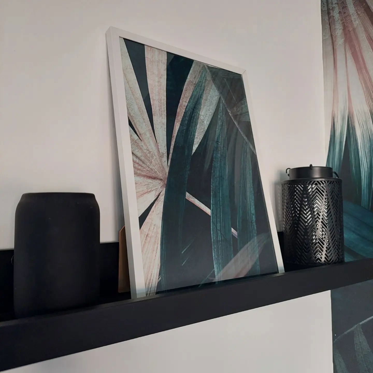 Półka z oprawioną grafiką botaniczną, czarnym wazonem i wzorzystym metalowym lampionem.