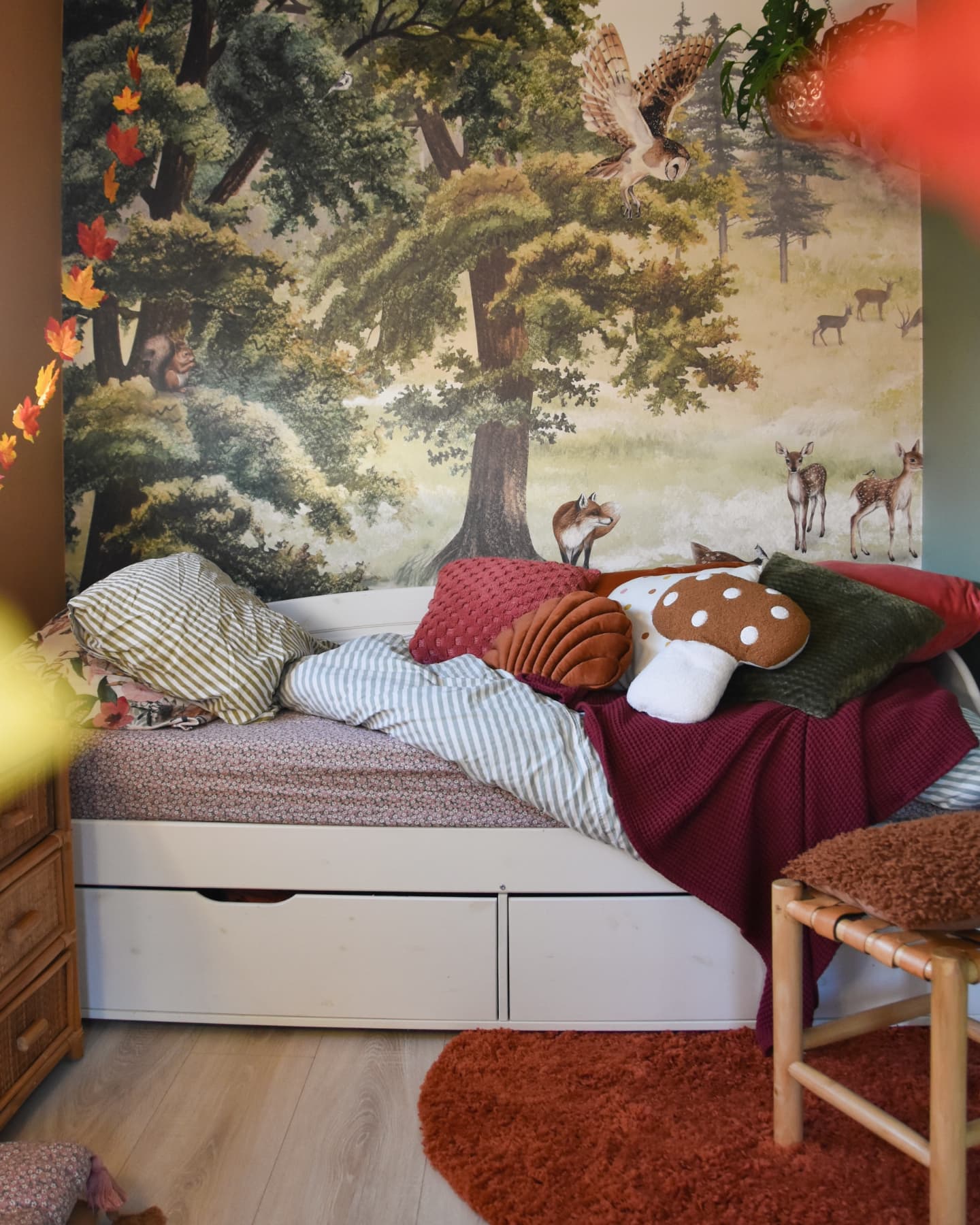 Chambre d'enfant avec une murale de forêt, un lit gigogne blanc et un oreiller en forme de champignon.