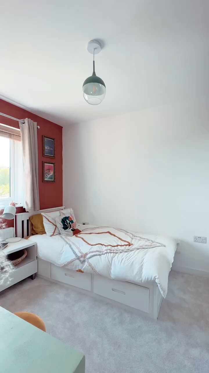 Bedroom with white single bed, storage drawers, rust accent wall, and globe pendant light.