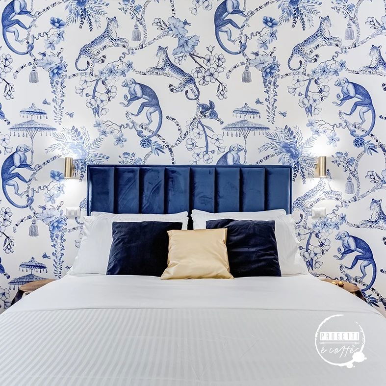 Bedroom with blue velvet headboard, white bedding, and monkey and leopard print wallpaper.