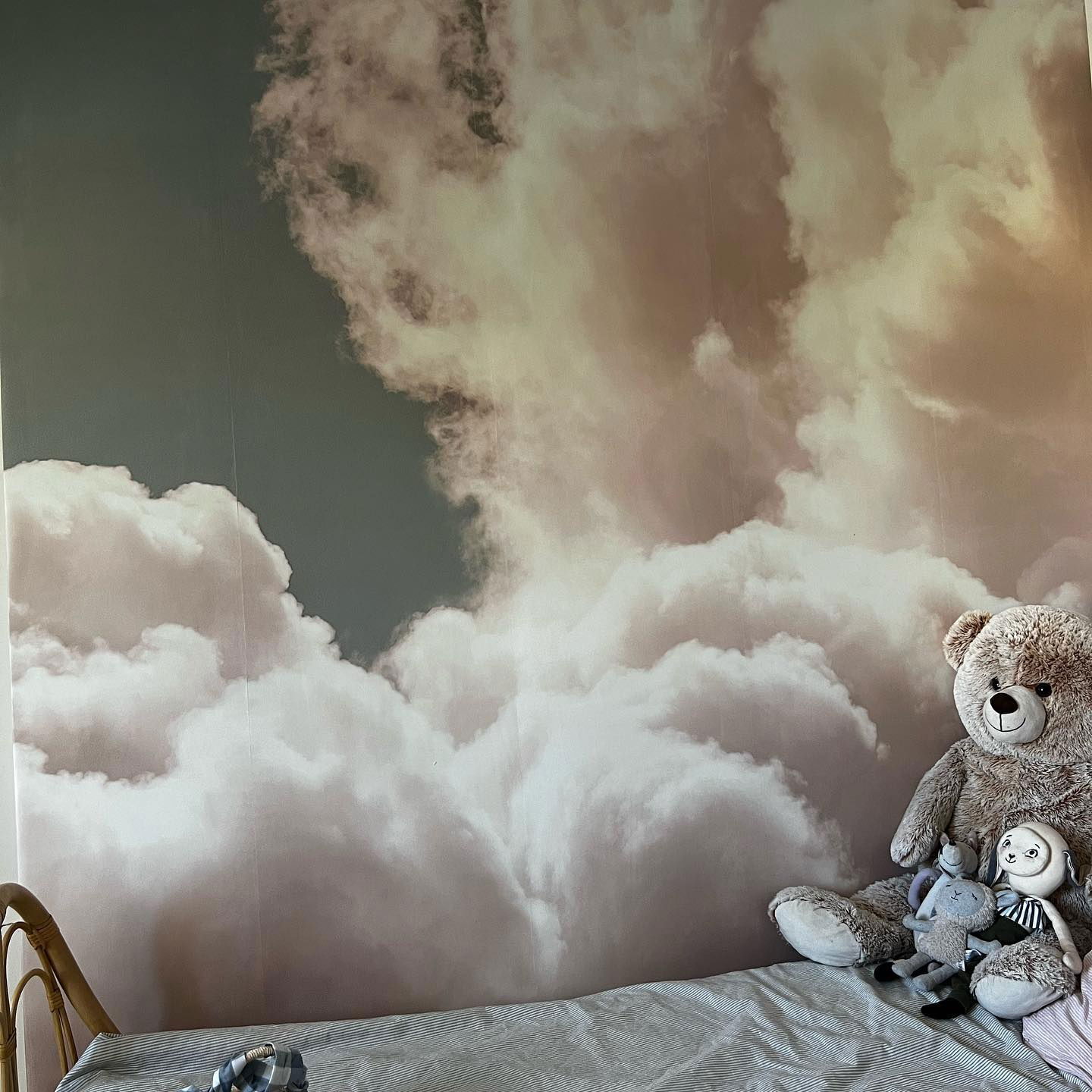 Child's room with cloud wallpaper, bed, and stuffed animals.