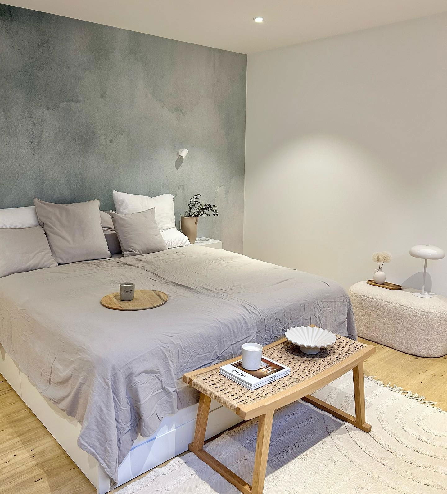 Bedroom with gray bedding, watercolor accent wall, and light wood bedside table.