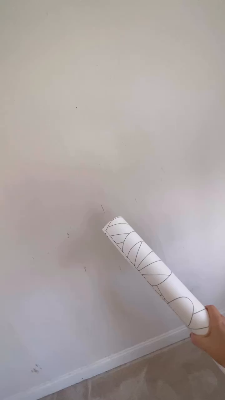 Hand holding roll of white wallpaper with gray geometric pattern against white wall.