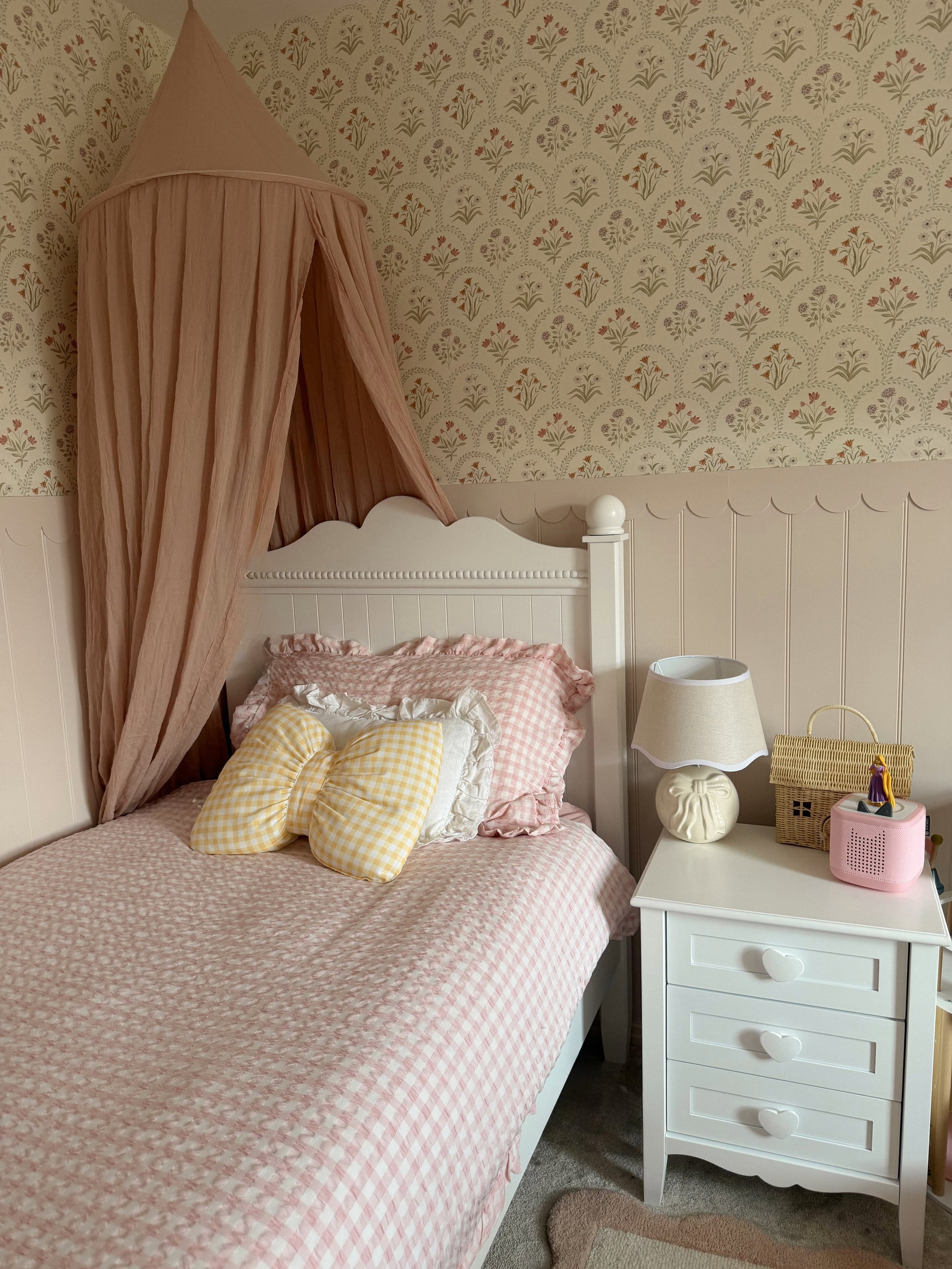 Una cama infantil con ropa de cama de cuadros rosas, un dosel rosa y cojines decorativos.
