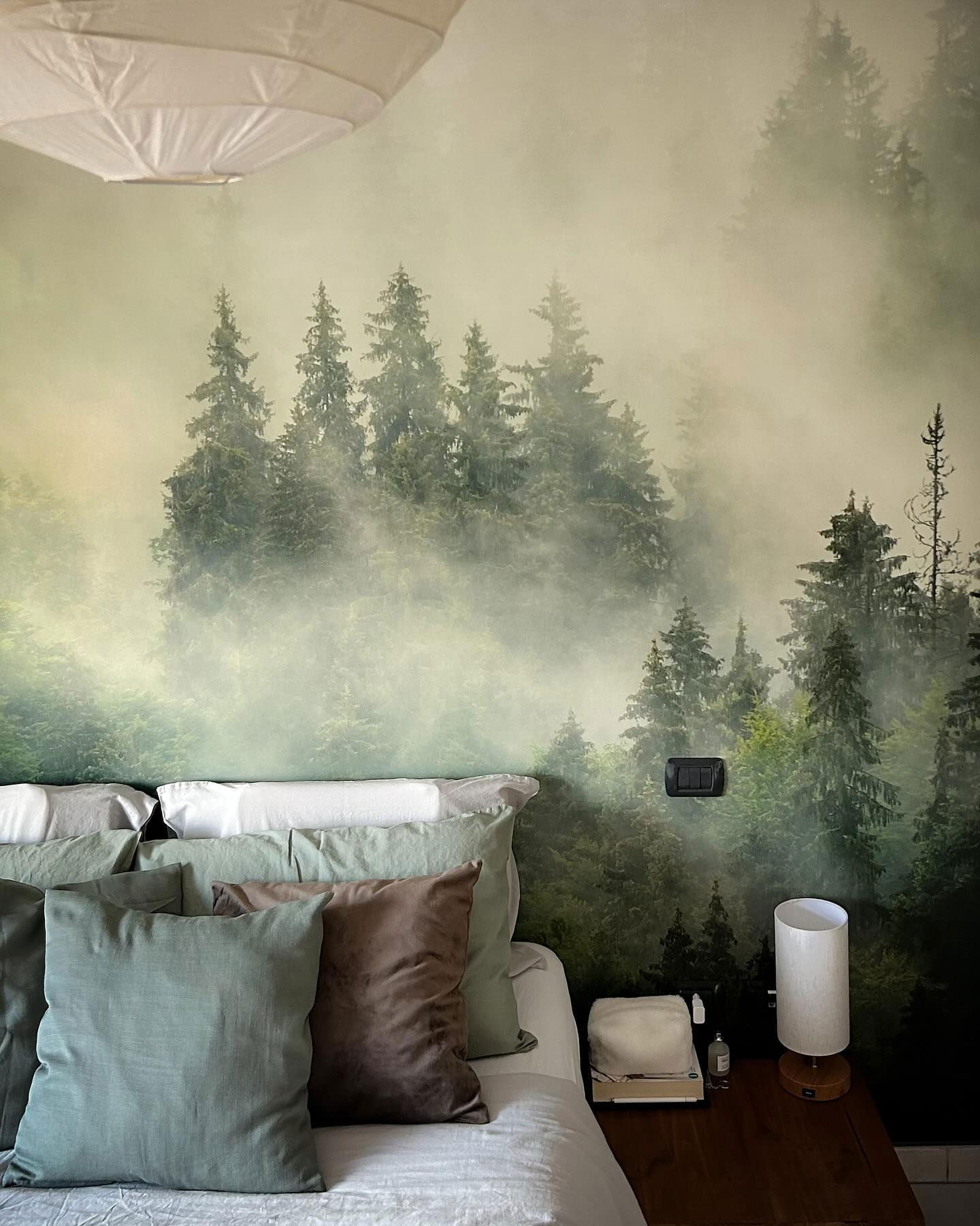 Bedroom with forest mural, bed with green and brown pillows, and white paper lantern.