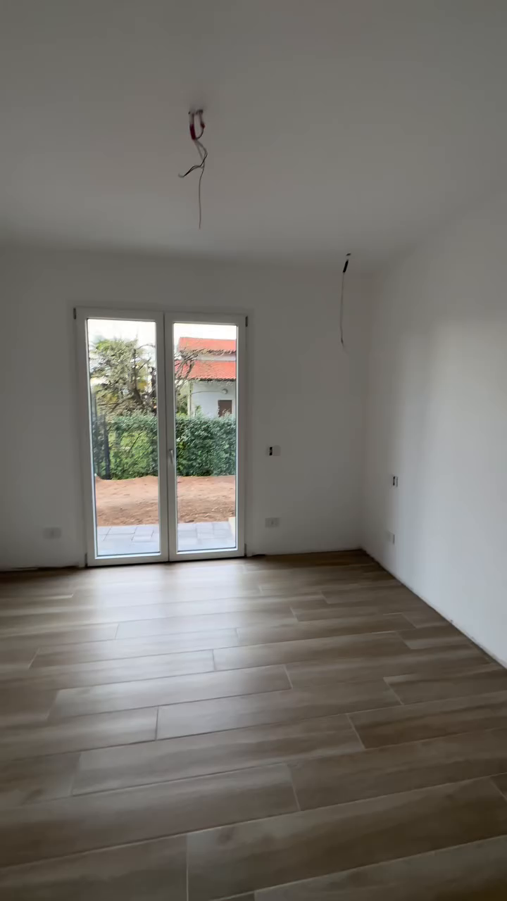 Bright room with wood-look tile flooring and white walls. Double doors lead to a yard.