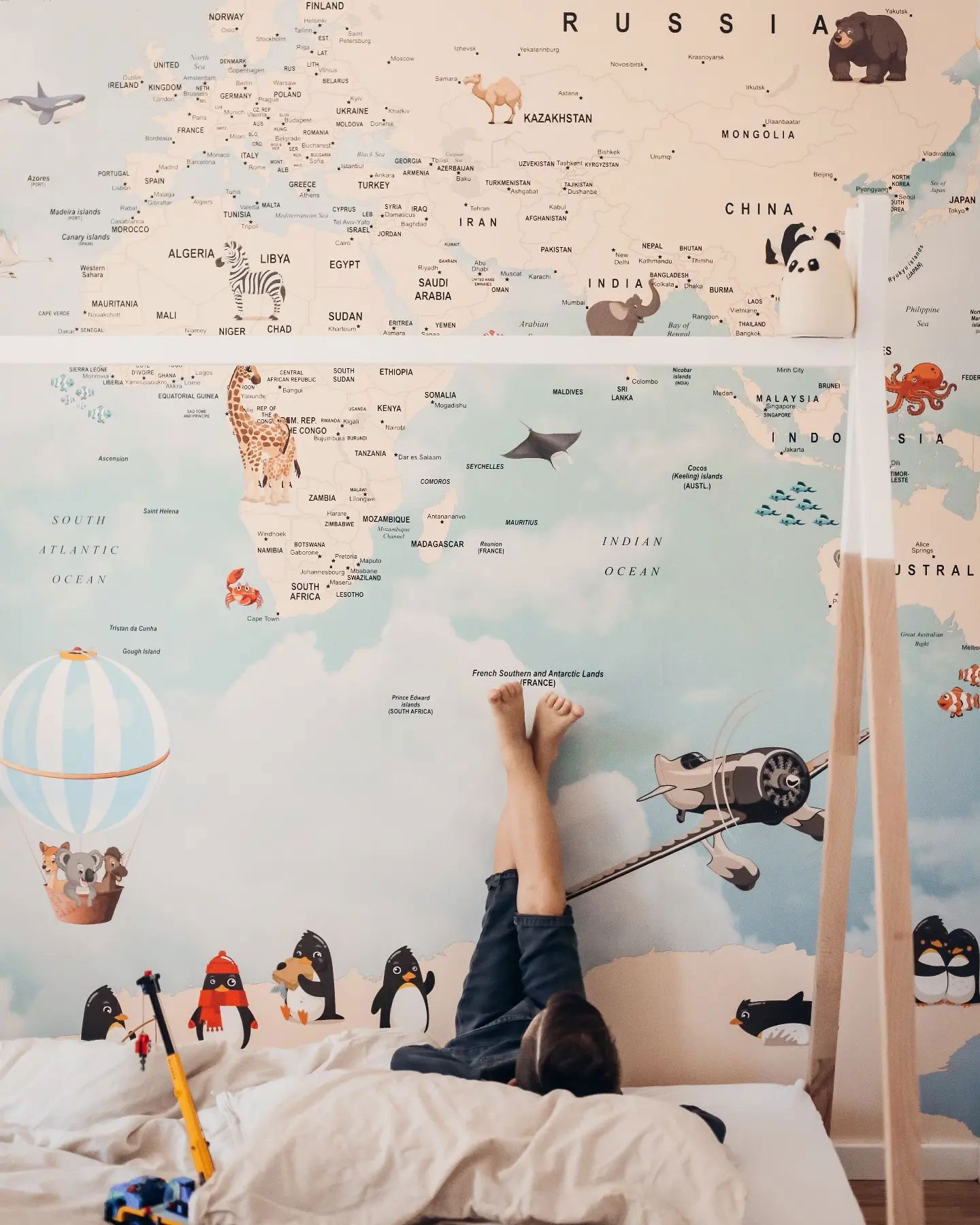 Bambino sdraiato sul letto con i piedi appoggiati a una decalcomania da parete con la mappa del mondo in una camera da letto giocosa.