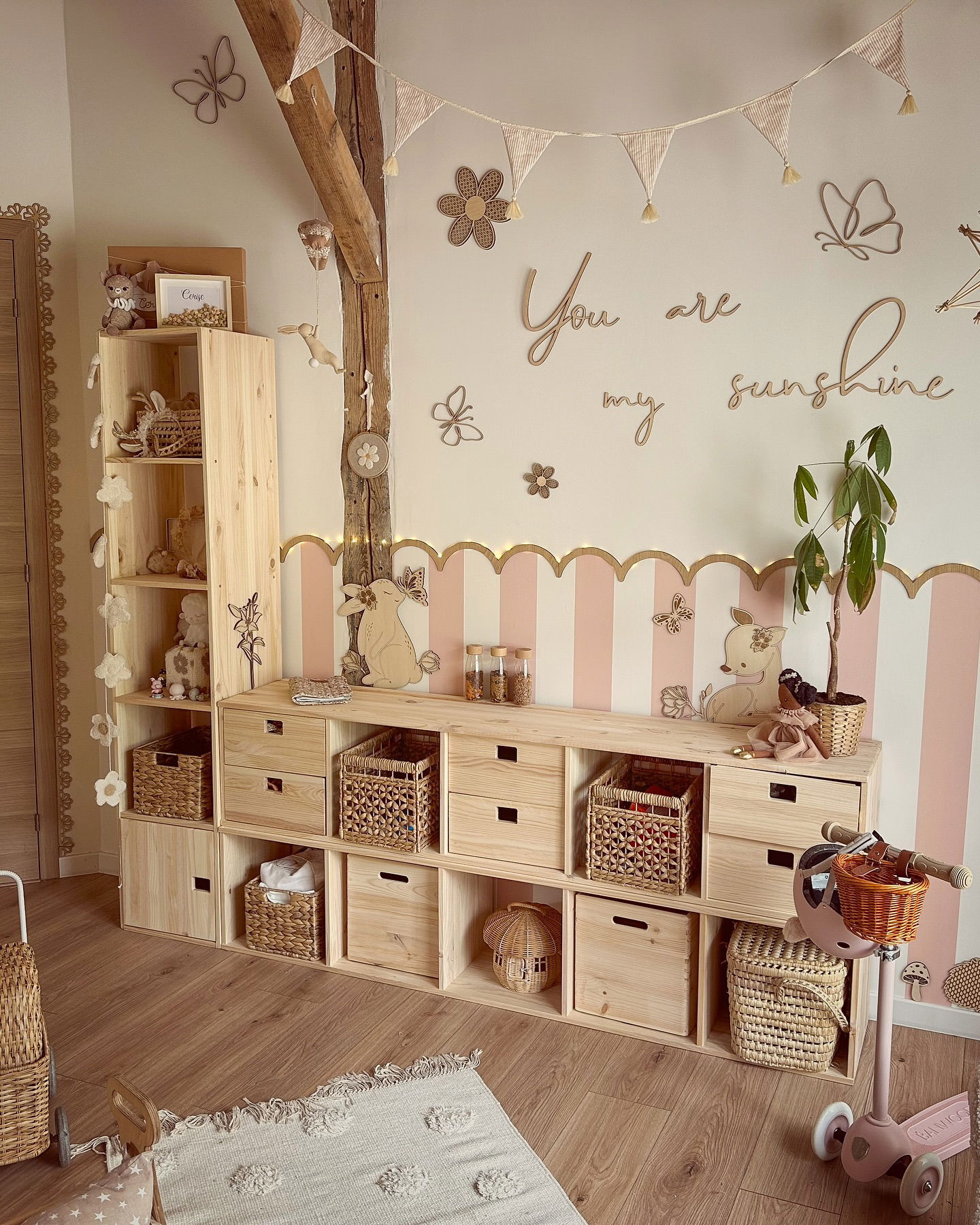 Kinderzimmer mit hölzernen Aufbewahrungsregalen, Körben und Schubladen. Die Wandkunst umfasst "You are my sunshine" und Schmetterlingsaufkleber.