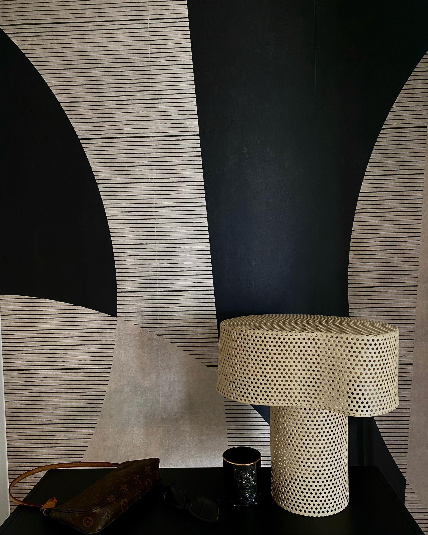 Modern interior with patterned wallpaper, perforated metal lamp, and Louis Vuitton purse.