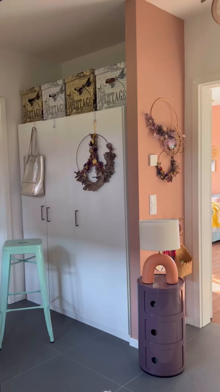 Hallway with white storage cabinet, floral wreaths, and purple dresser with lamp.