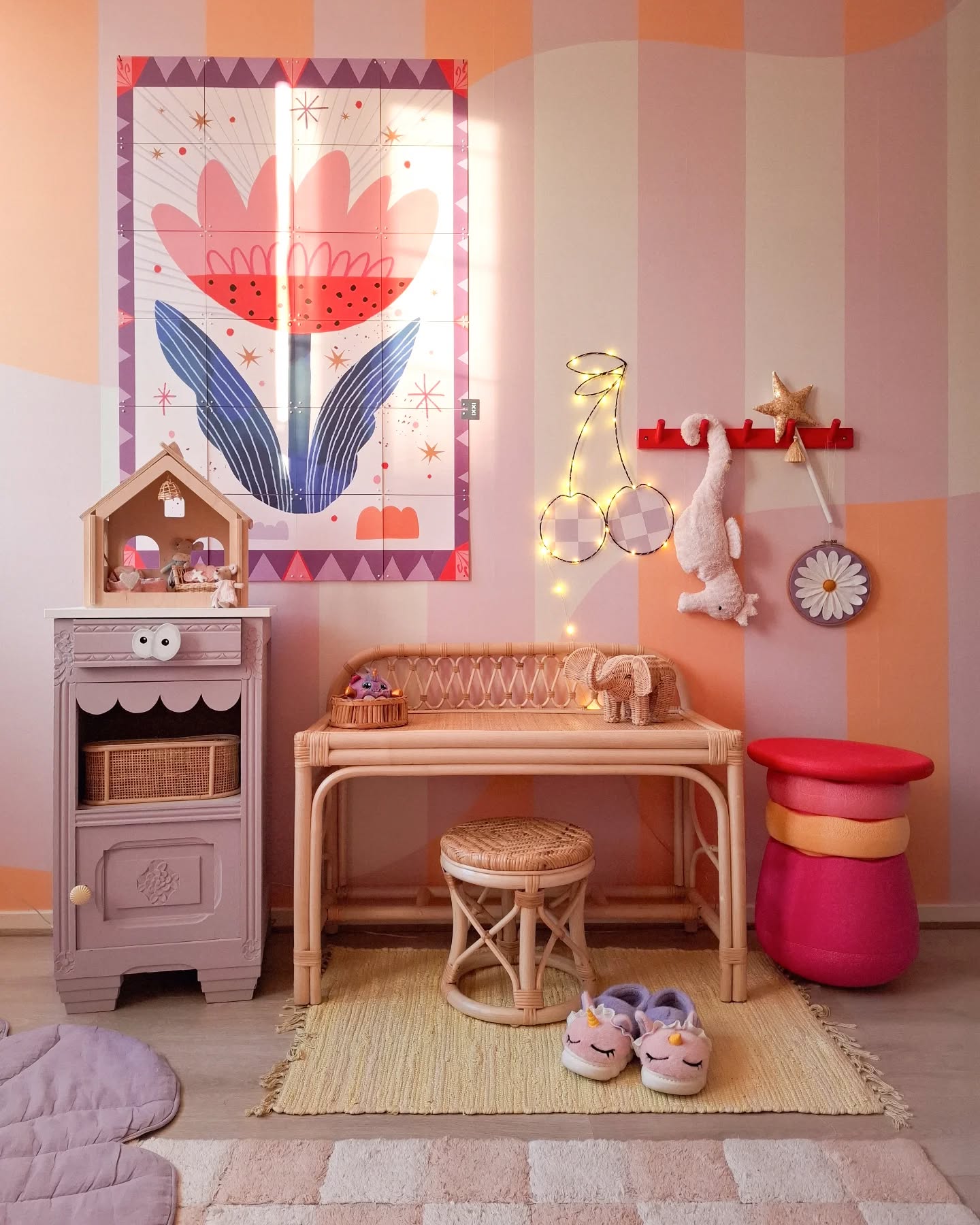 A child's whimsical room with a large floral mural, rattan desk and stool, and colorful decor.