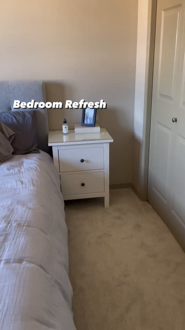 Bedroom with gray bedding, white nightstand, framed photo, and beige carpet.
