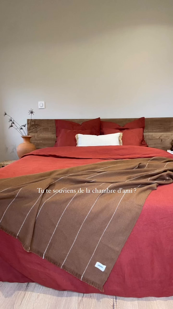 Bedroom with red bedding, wood headboard, and brown striped throw blanket.