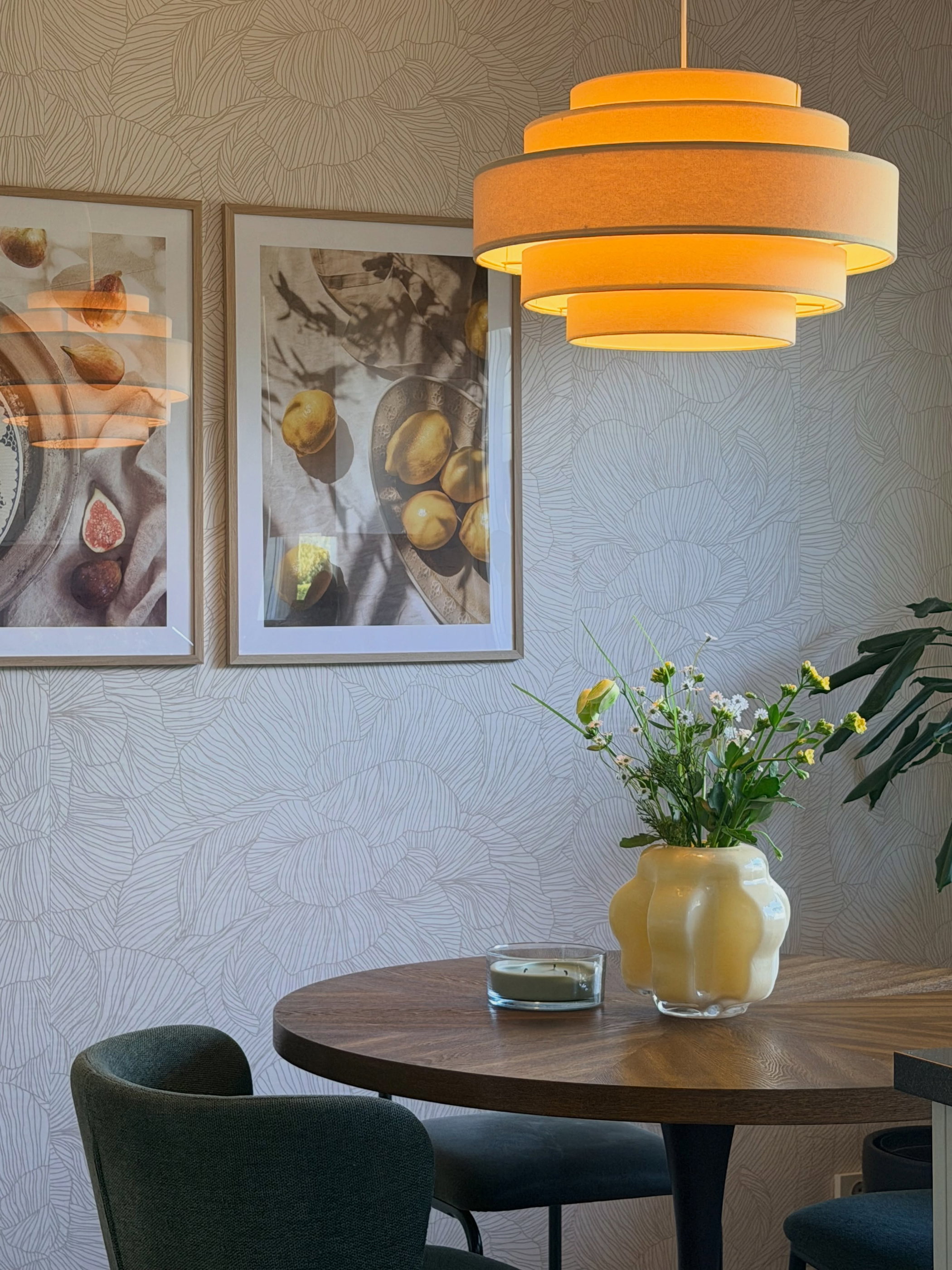 Round wooden table with floral vase, candle, and two framed fruit prints.