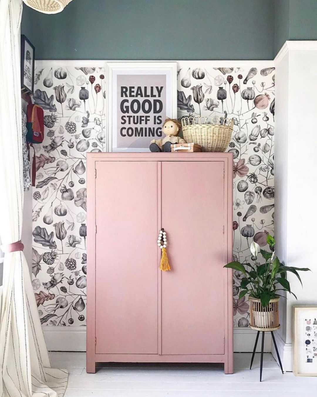 Interior with pink wardrobe, floral wallpaper, and "Really Good Stuff Is Coming" print.