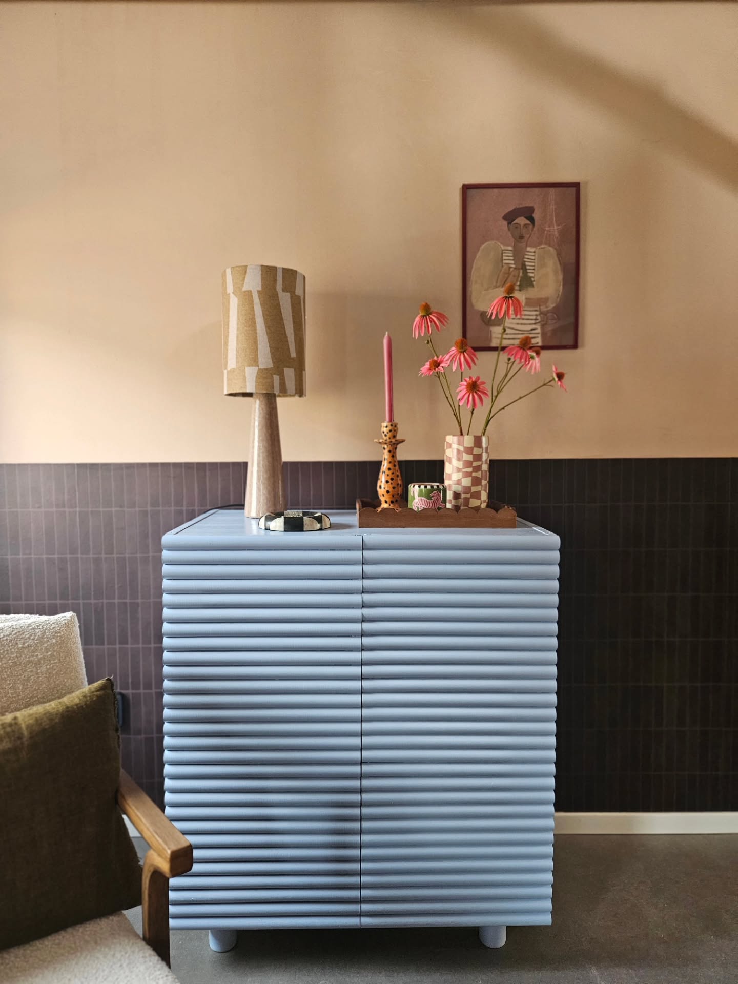 Mobiletto blu chiaro con ante a coste sormontato da una lampada, fiori, candela e un quadro.
