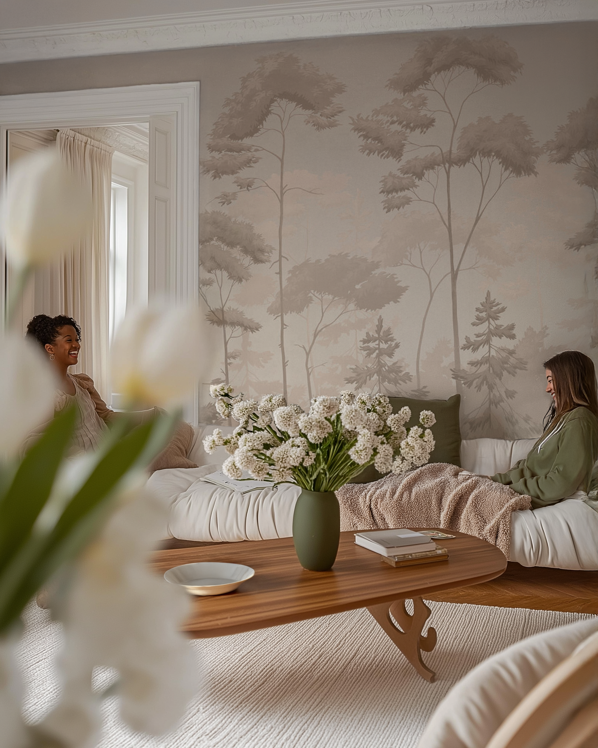 Living room with forest mural, wood coffee table, and two women on a white sofa.