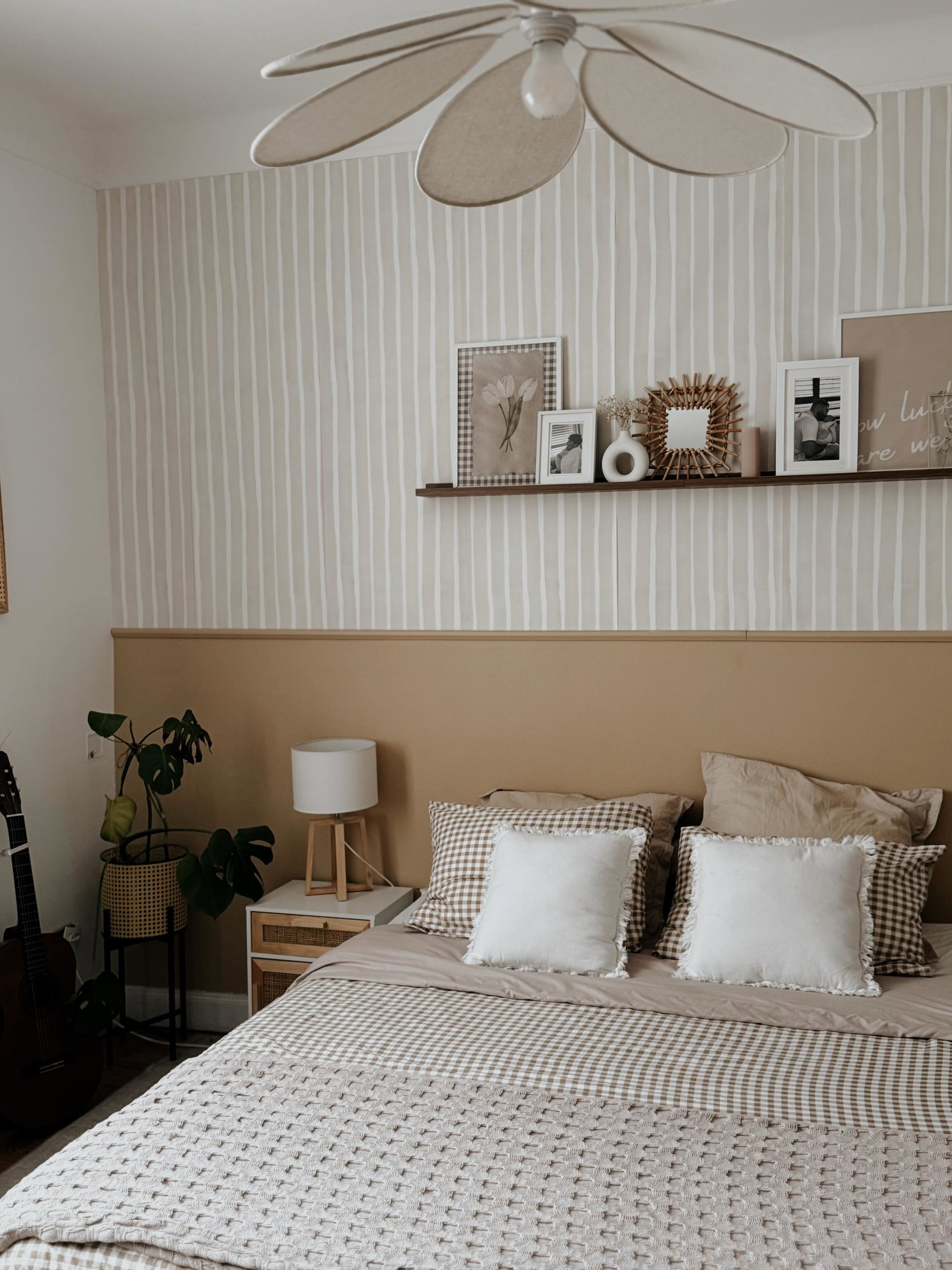 Gemütliches Schlafzimmer mit gestreifter Tapete, einem Bett mit gemusterten Bettwäsche und einem Regal mit gerahmten Fotos.