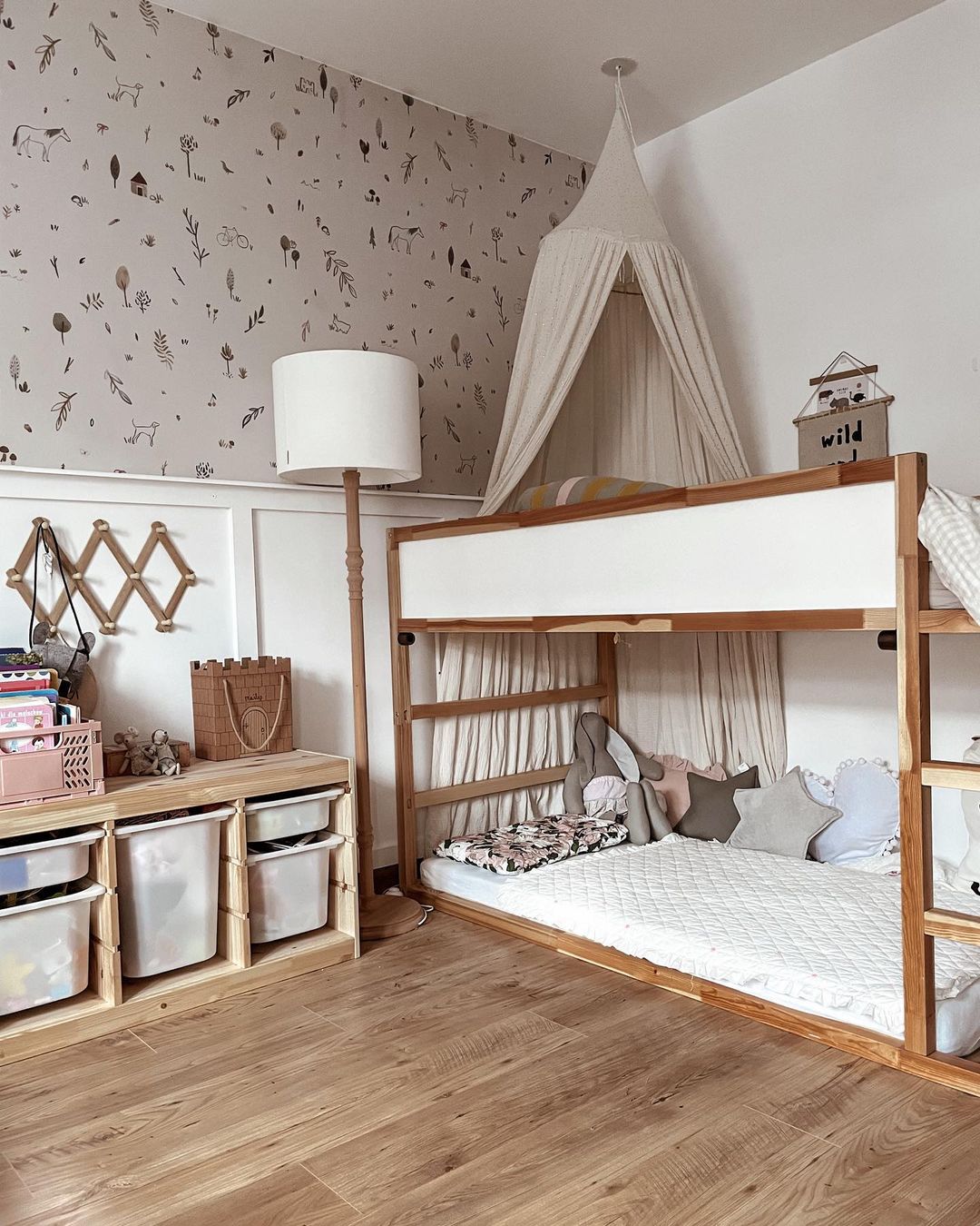 Camera da letto per bambini con letto a castello in legno, baldacchino e mobile contenitore con contenitori. Carta da parati con motivi di animali e natura.