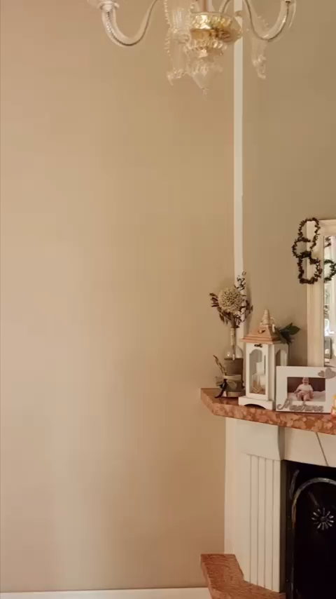 Interior view of a beige wall with a decorative fireplace and glass chandelier.