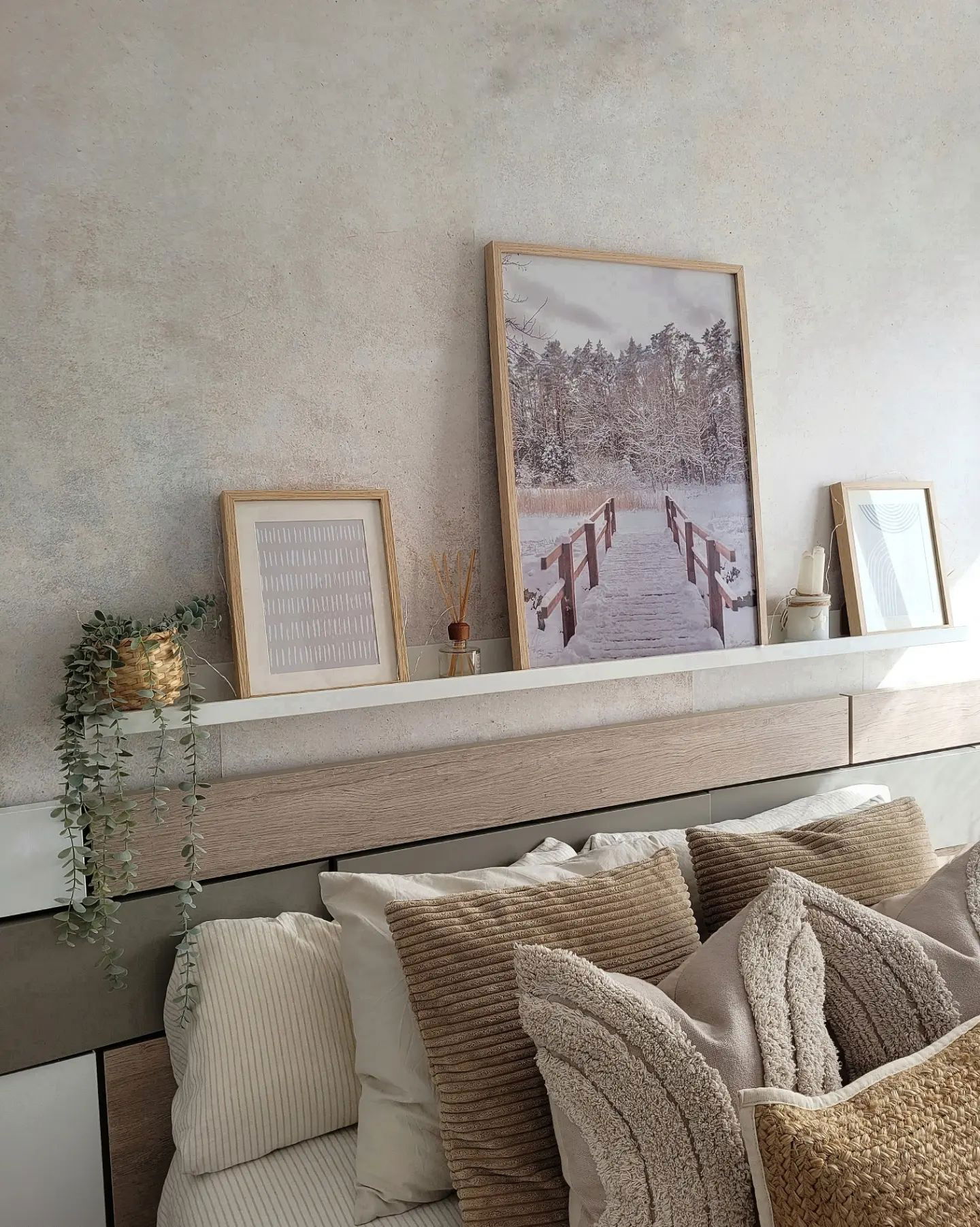 Schlafzimmerdekoration mit gerahmter Kunst, Pflanze und Kissen in neutralen Tönen.