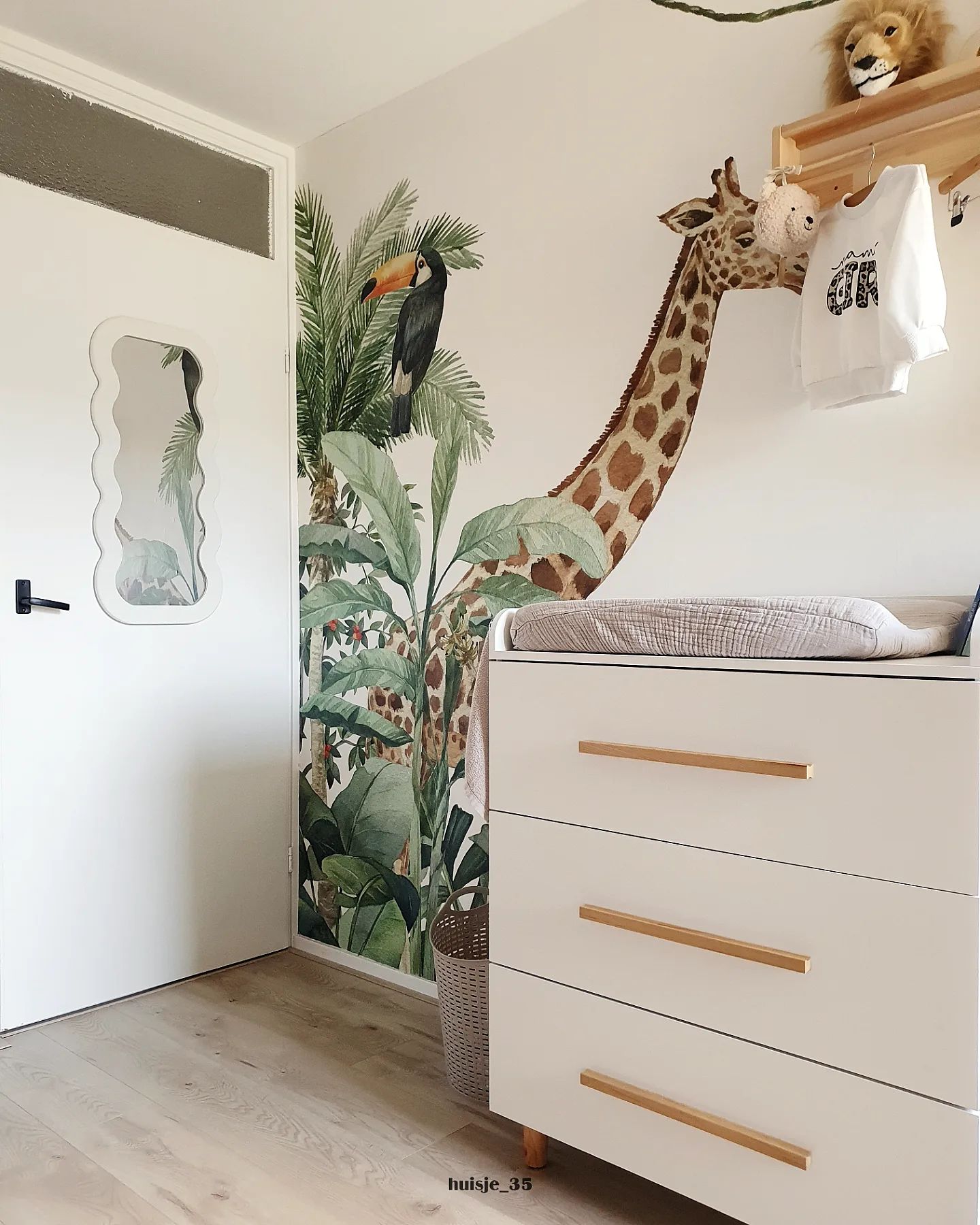 Nursery with giraffe wall decal, white changing table, and jungle-themed wallpaper.
