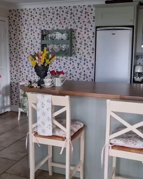 Kitchen interior with floral wallpaper, bar counter, and two white wooden bar stools.