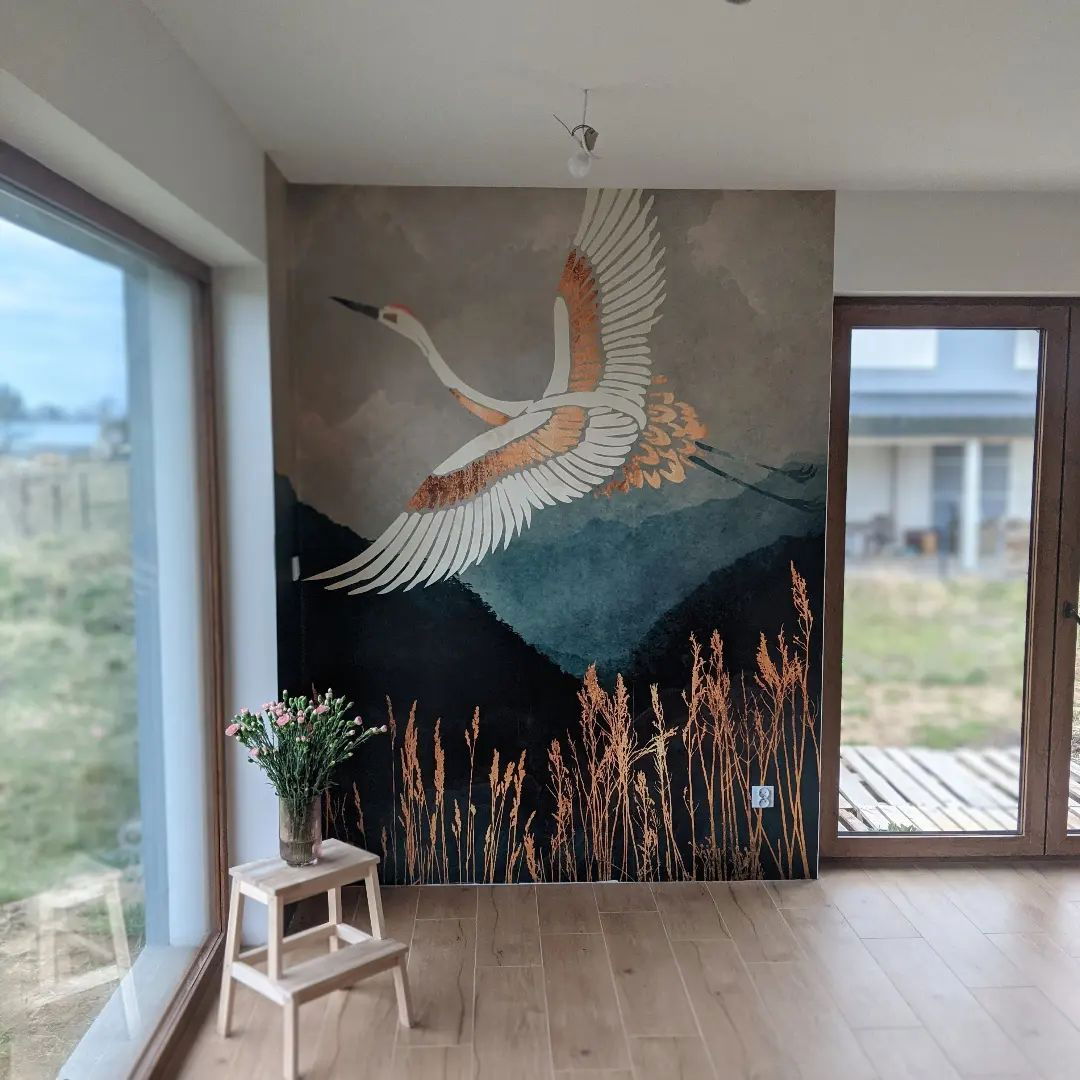 Interior with crane mural, wood floors, and natural light. A small stool with flowers sits near a large window.