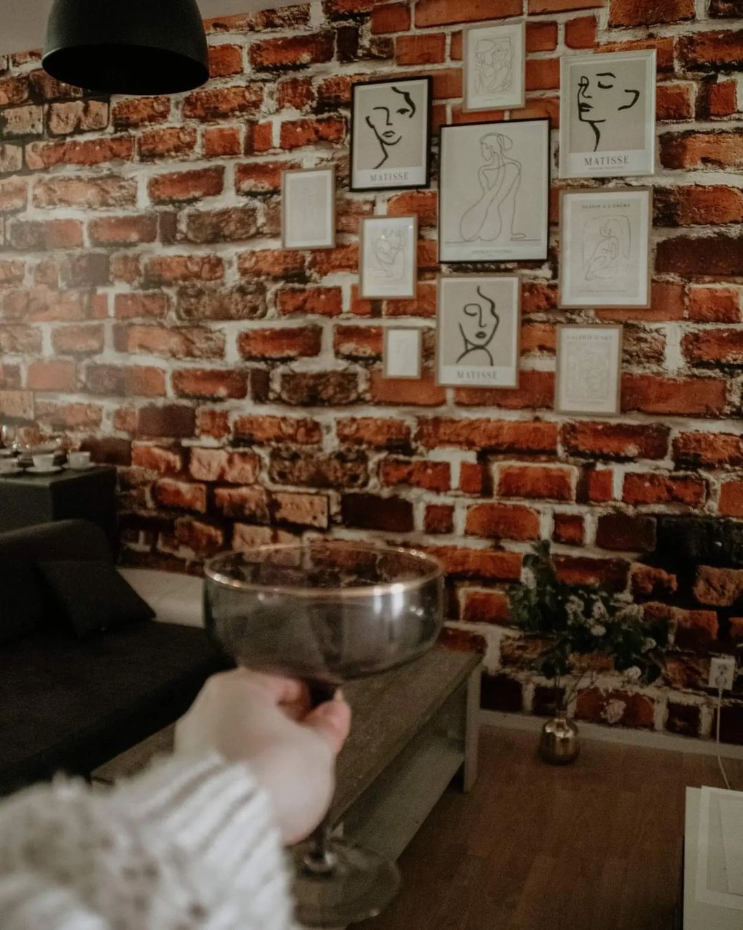 Interior with brick wall, Matisse art prints, and hand holding coupe glass.
