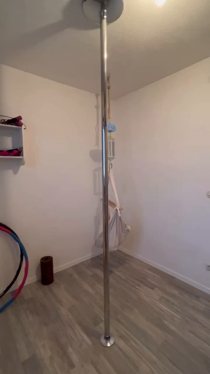 Indoor view of a chrome dance pole installed in a room with light gray wood floors.