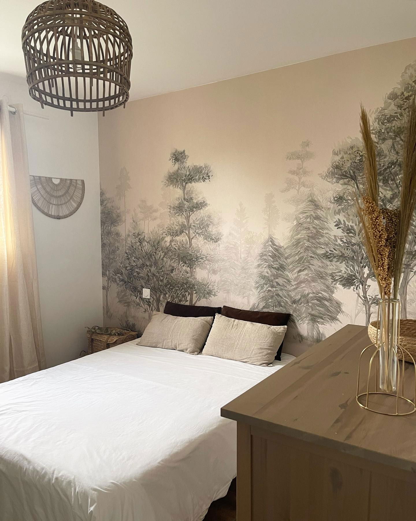 Bedroom with white linens, tree mural, and woven light fixture.