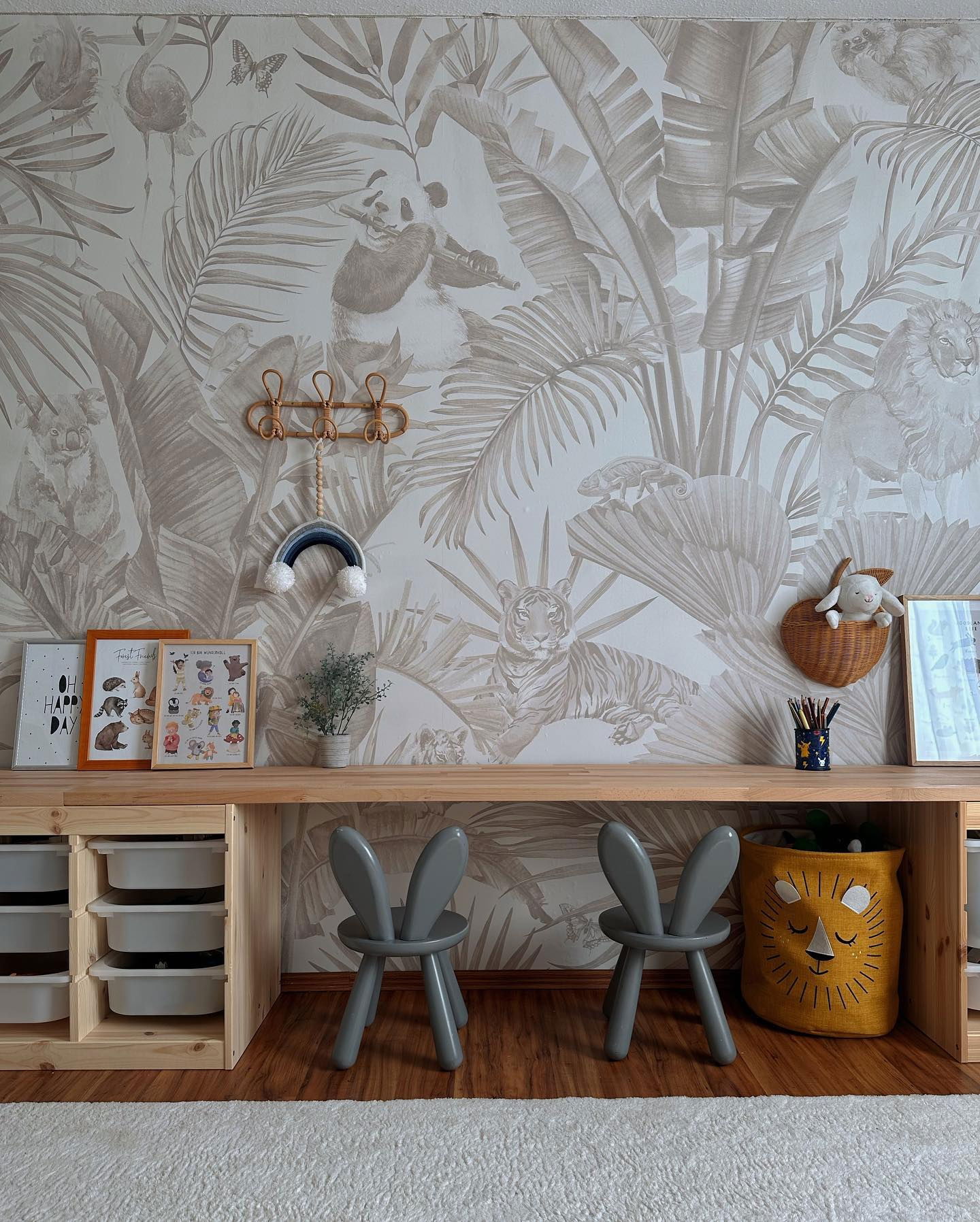 Salle de jeux pour enfants avec papier peint jungle, bureau en bois et chaises lapin grises.