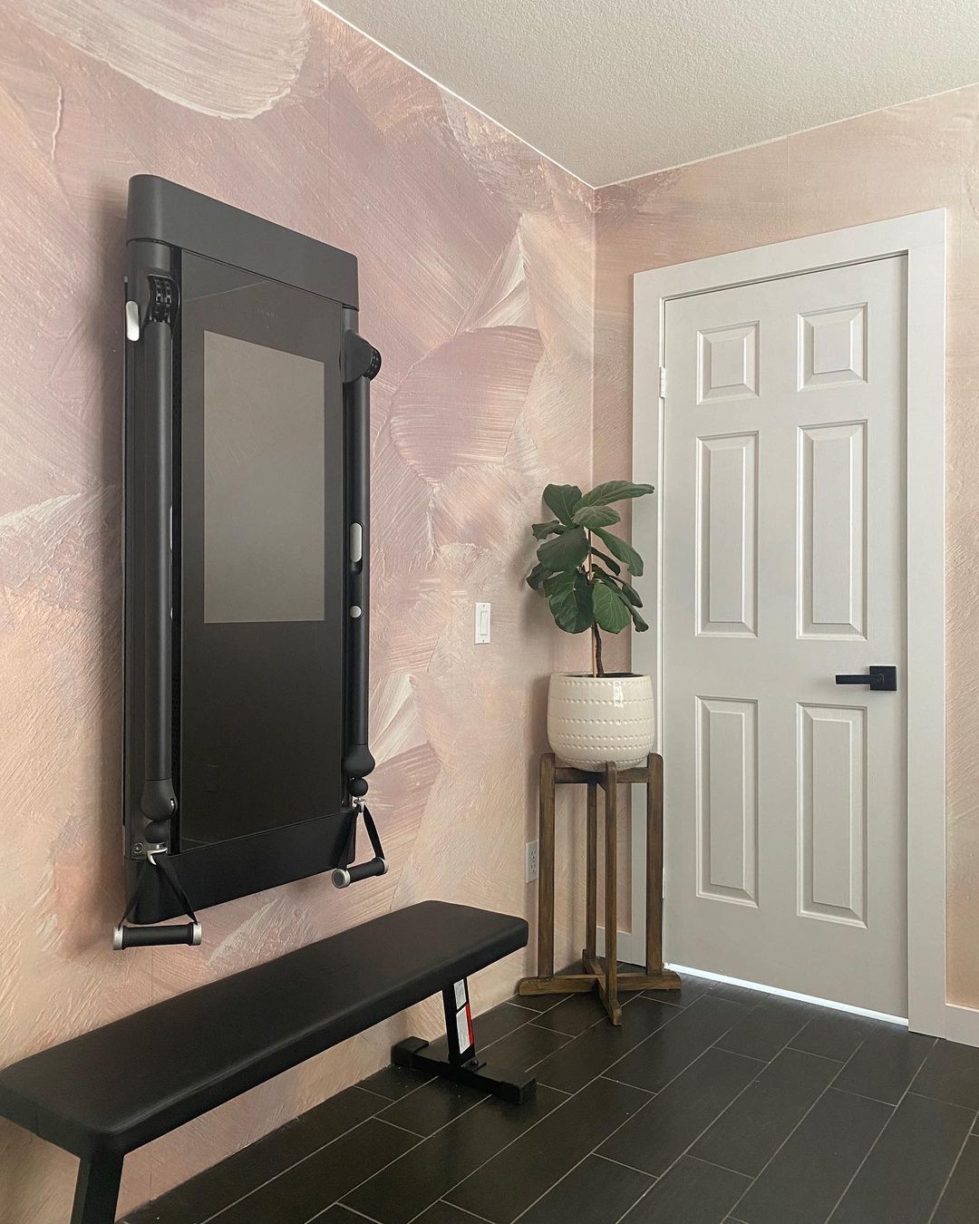 Home gym featuring Tonal machine, workout bench, and potted plant against a pink painted wall.