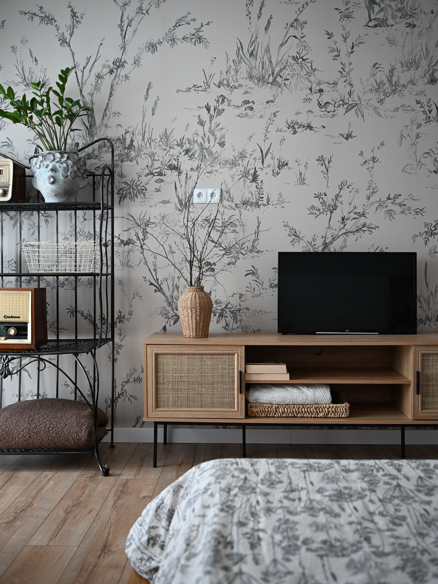 Wood media console with woven cabinet door, TV, and decorative items in a room with floral wallpaper.