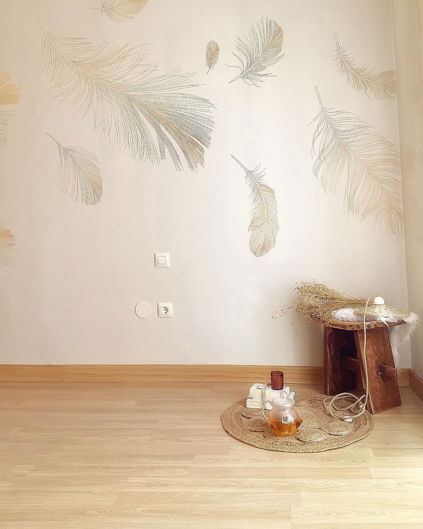 Rincón acogedor de una habitación con arte de pared de plumas, juego de té sobre una alfombra de yute y taburete de madera con flores secas.