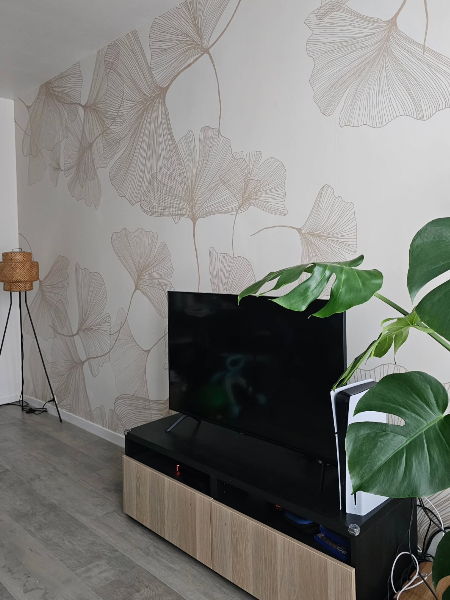 Nowoczesny salon z dużym telewizorem, minimalistyczną szafką RTV i tapetą z subtelnym wzorem liści.