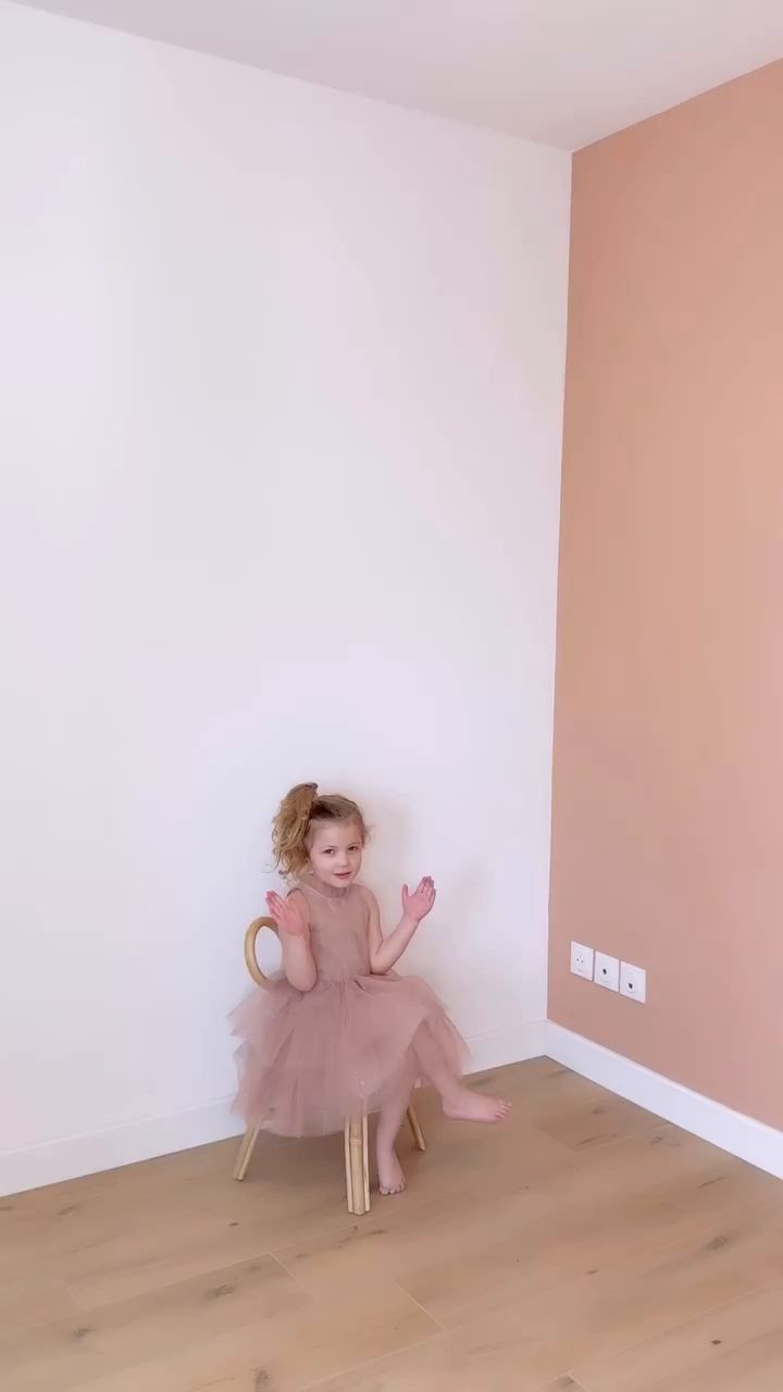 A young girl in a pink tulle dress sits on a small chair.