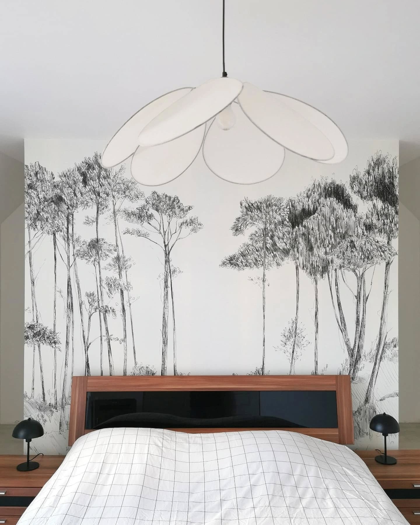 Bedroom with a white flower pendant light, bed with grid pattern, and forest mural.