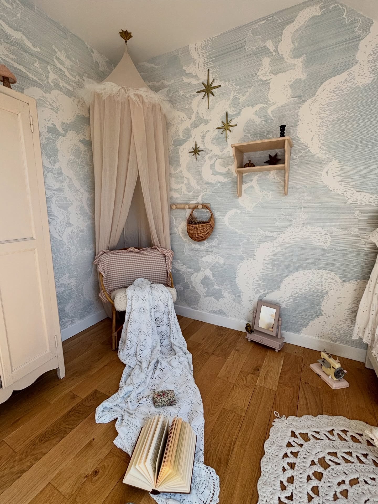 Bedroom with cloud wallpaper, canopy over chair, and an open book on the floor.