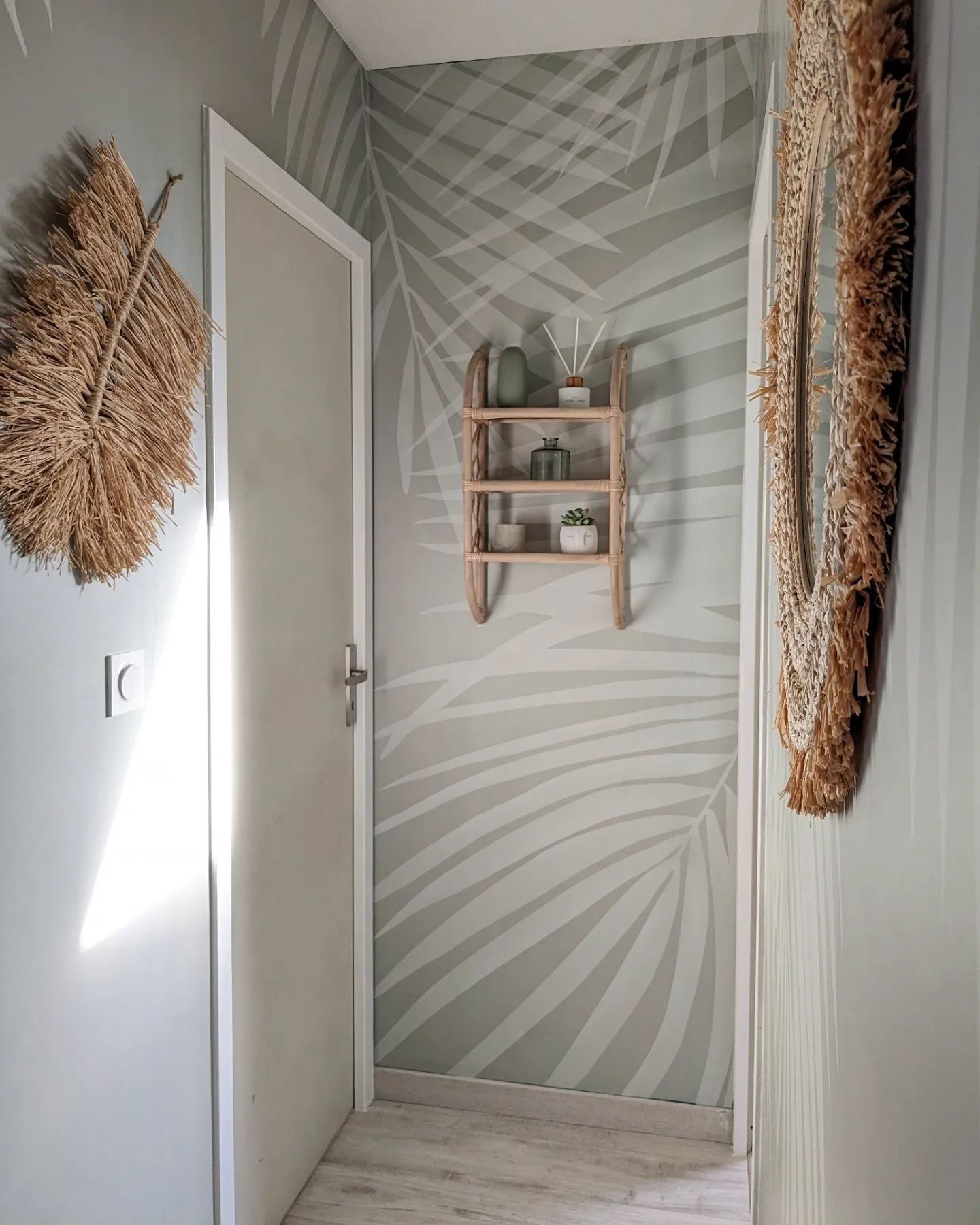 Hallway with palm leaf wallpaper, straw leaf decor, and a woven mirror.