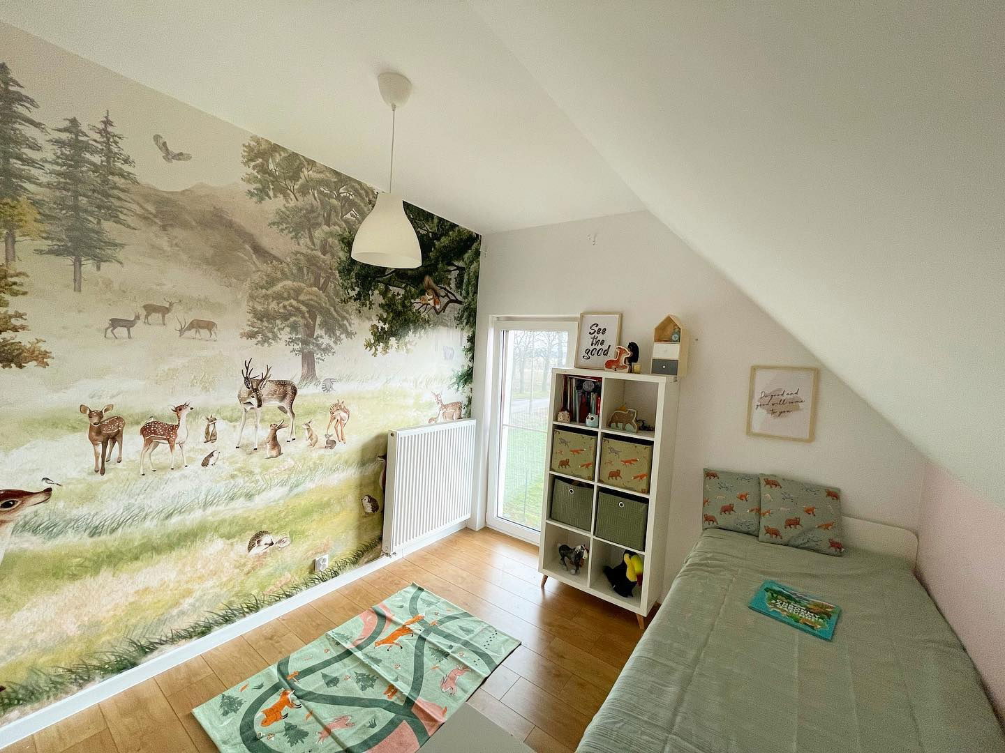 Chambre d'enfant avec une murale de forêt, des étagères blanches et un lit jumeau avec une literie verte.