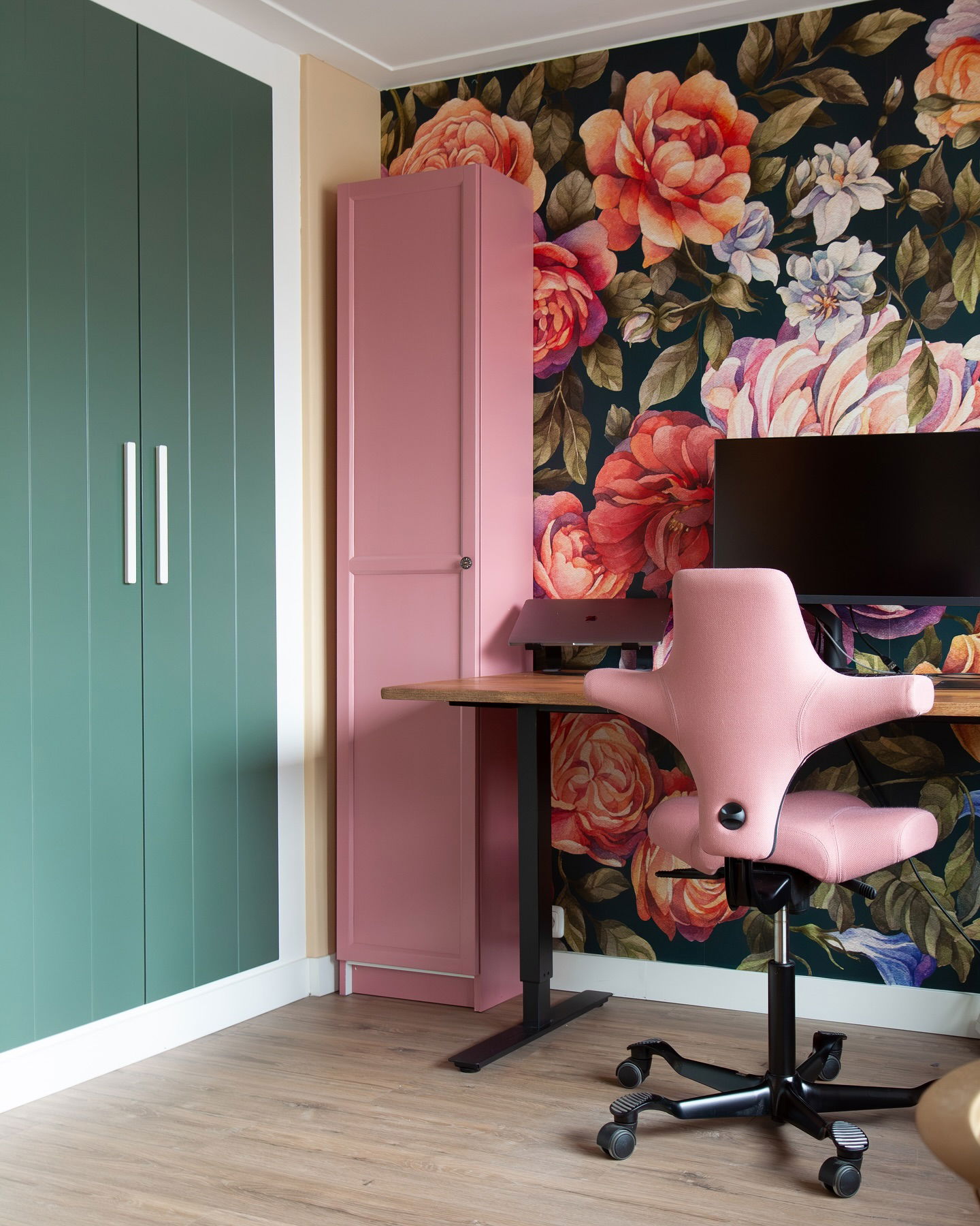 Interior with floral wallpaper, pink office chair, and standing desk.