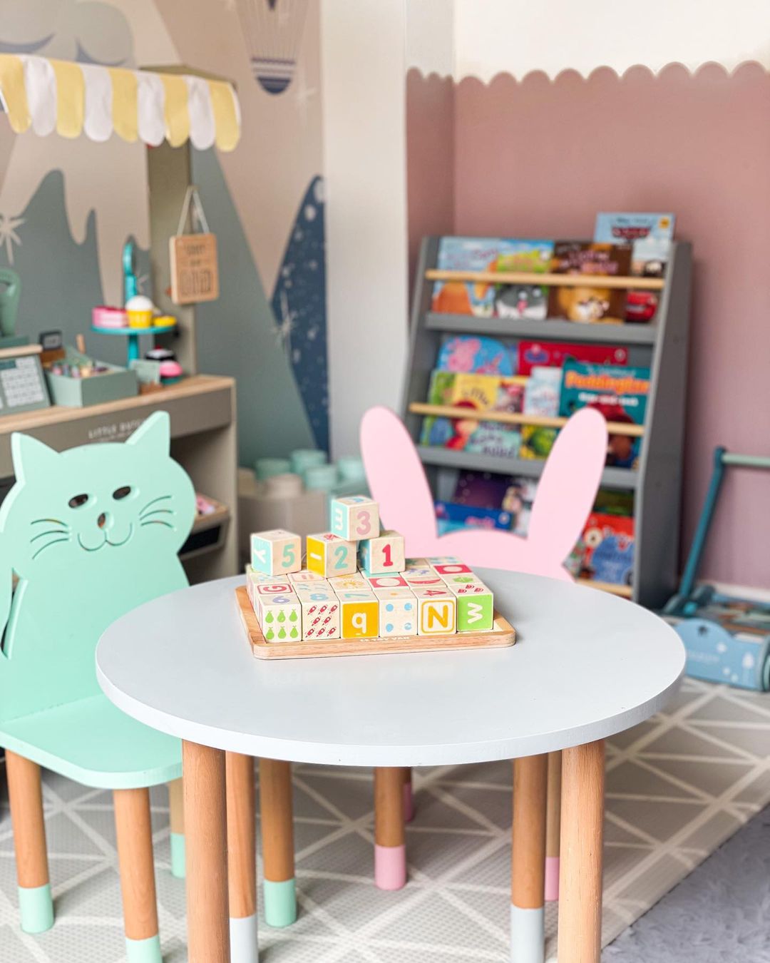 Playroom scene with alphabet blocks on a round table, cat-shaped chair, and bunny-eared chair.