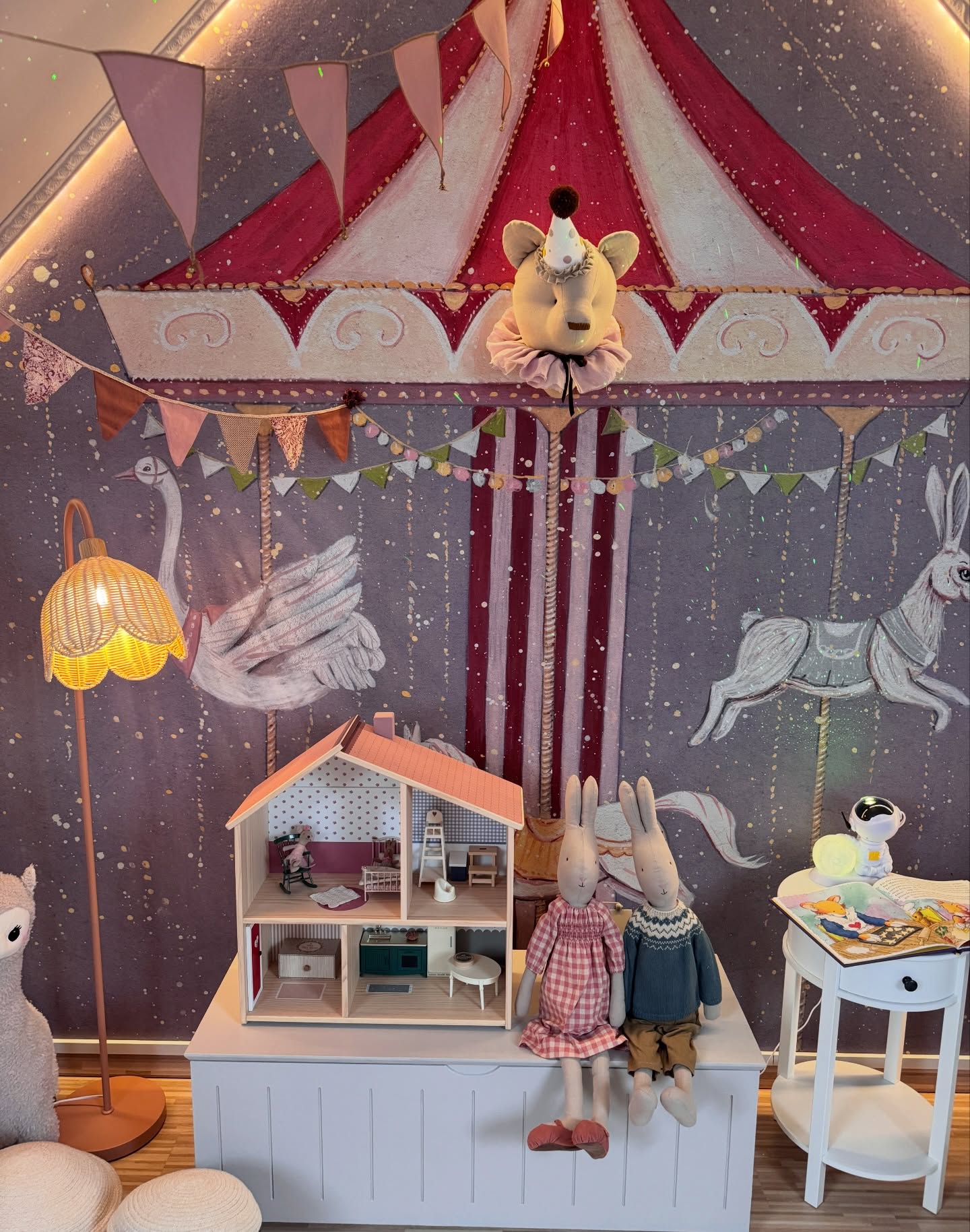 Dollhouse with two bunny dolls in front of a circus-themed mural.